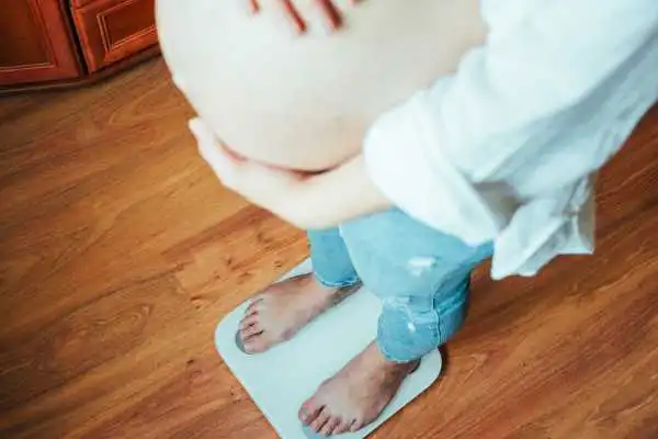 Image of woman weighing herself and experiencing weight gain through pregnancy Falkirk